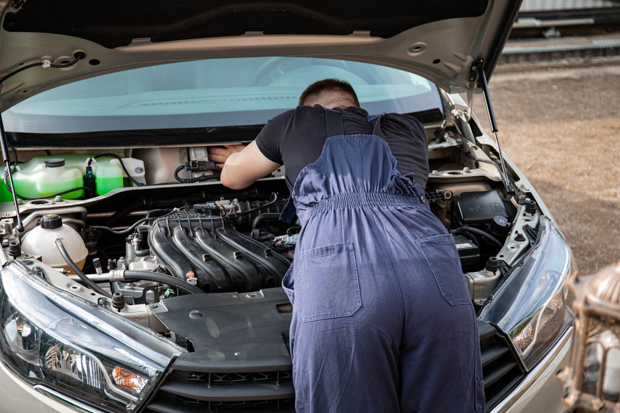An automotive mechanic performing engine maintenance on a car outdoors, showcasing mechanical skills.